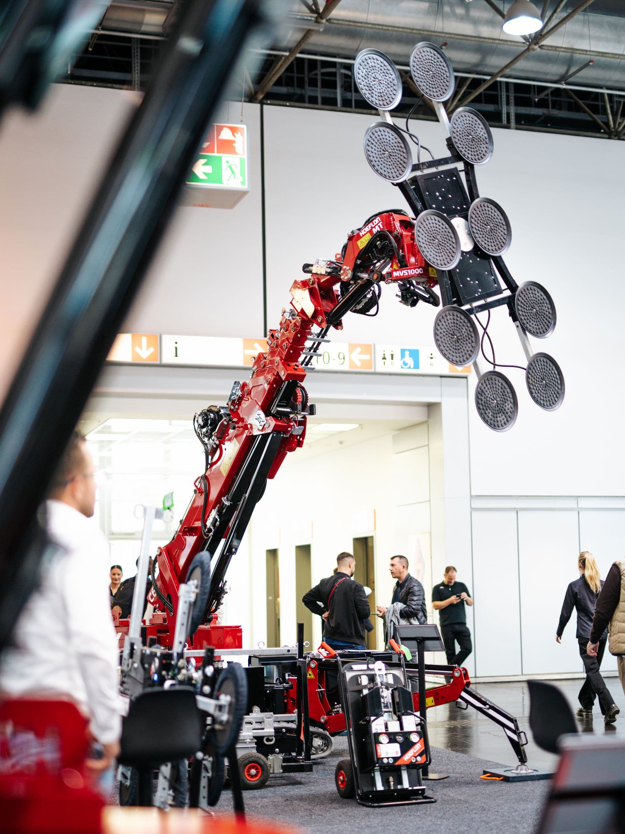 Hoeflon crane lifting an object with a glass suction device at a trade show.