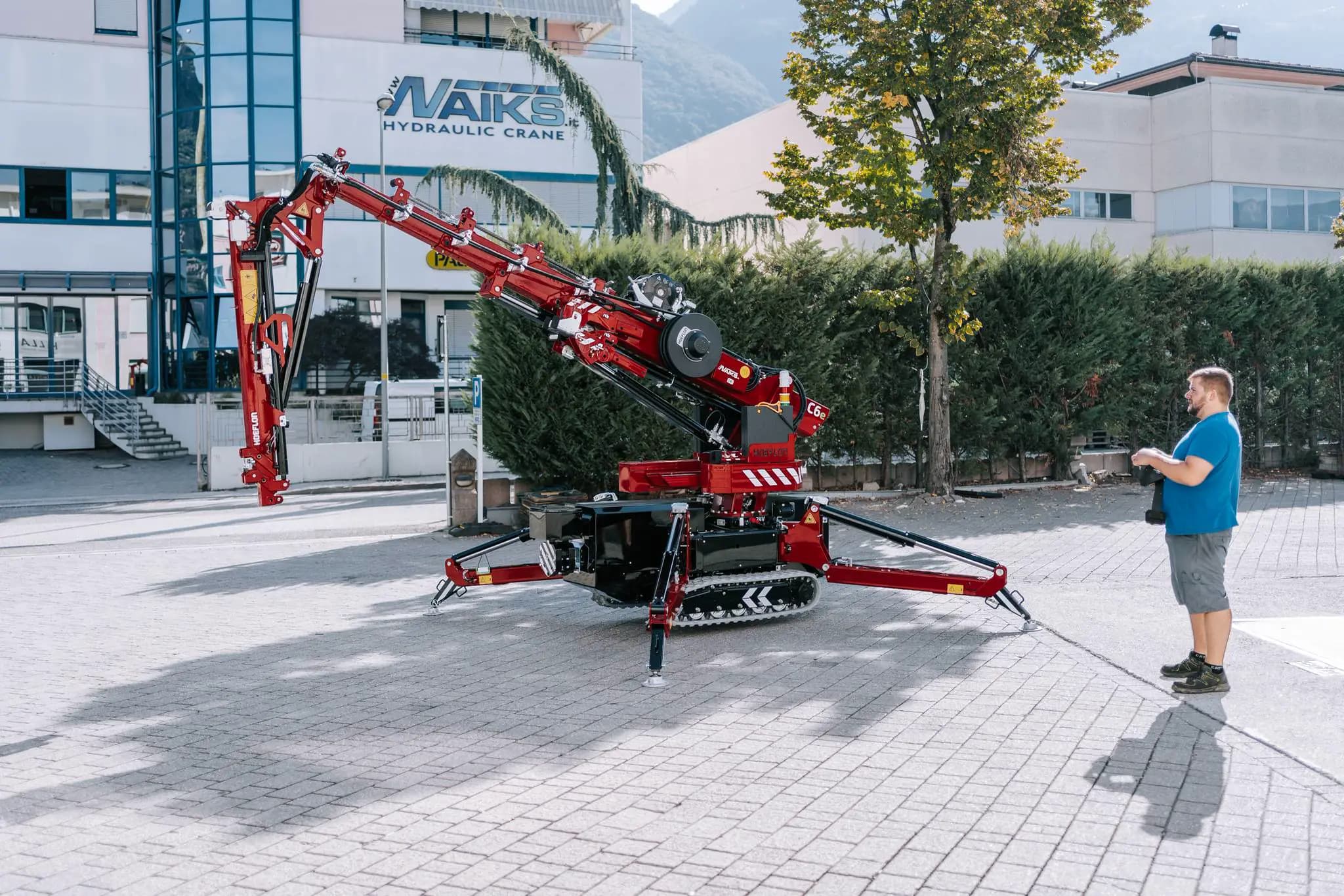 Hoeflon crane in action outside, man controls crane with remote panel.