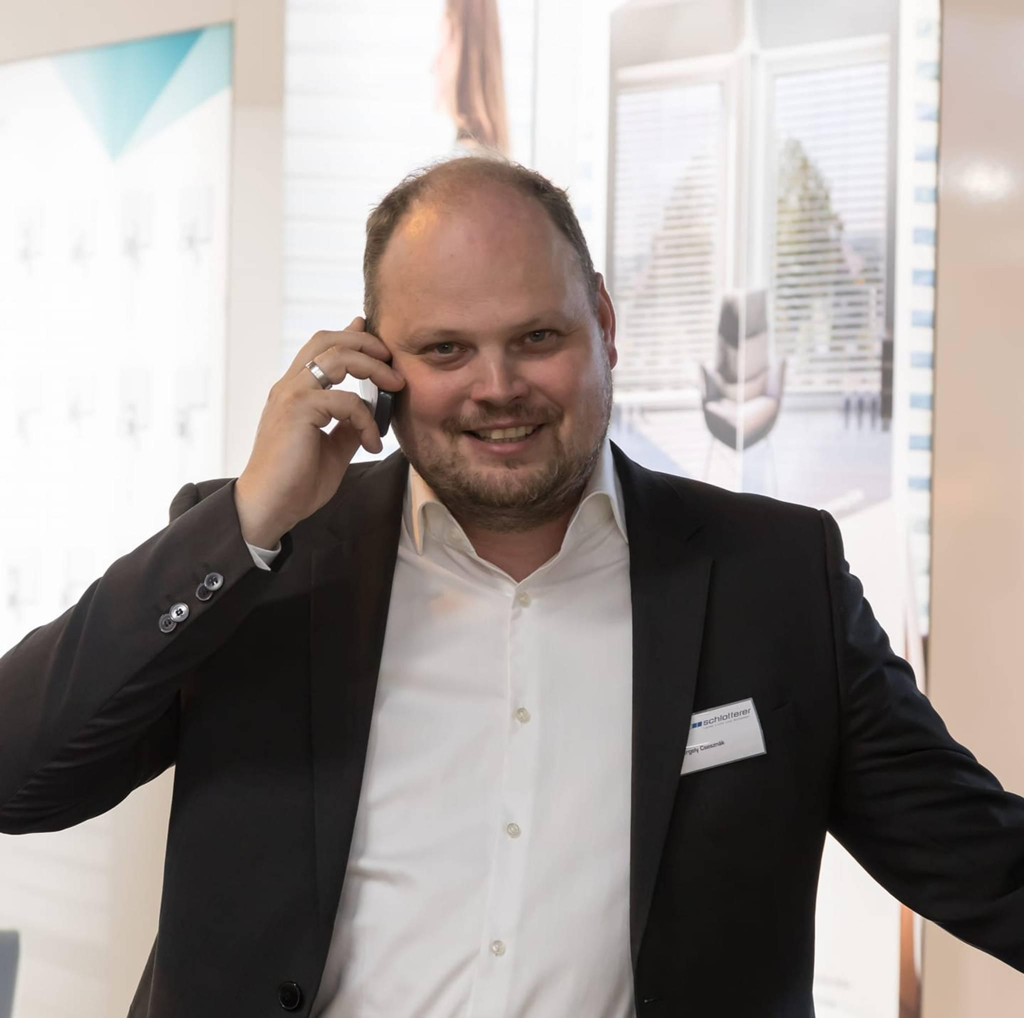 Gergely Metromont, man in a suit, talking on the phone at an exhibition.