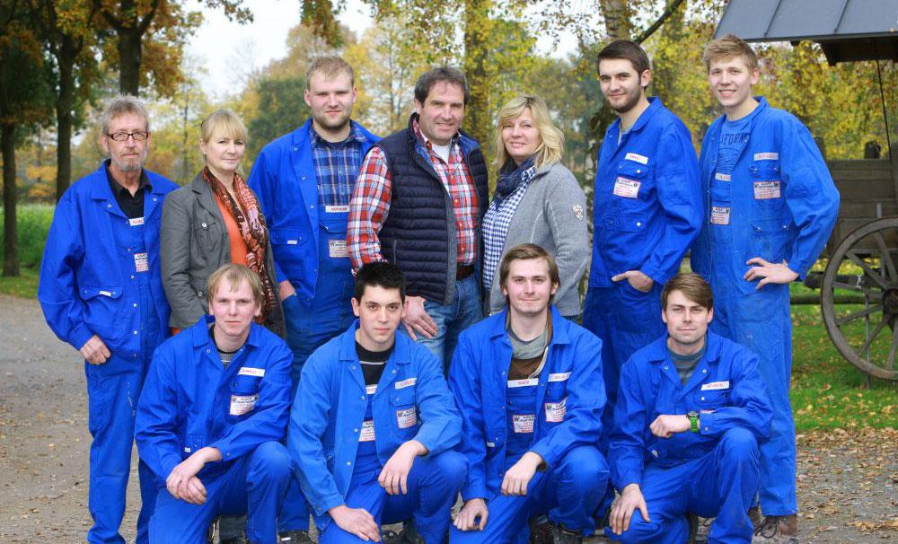 Group photo of employees in blue overalls, outdoors in nature.
